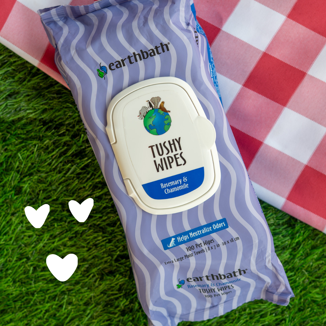 Earthbath Tushy Wipes package on grass with a checkered blanket in the background